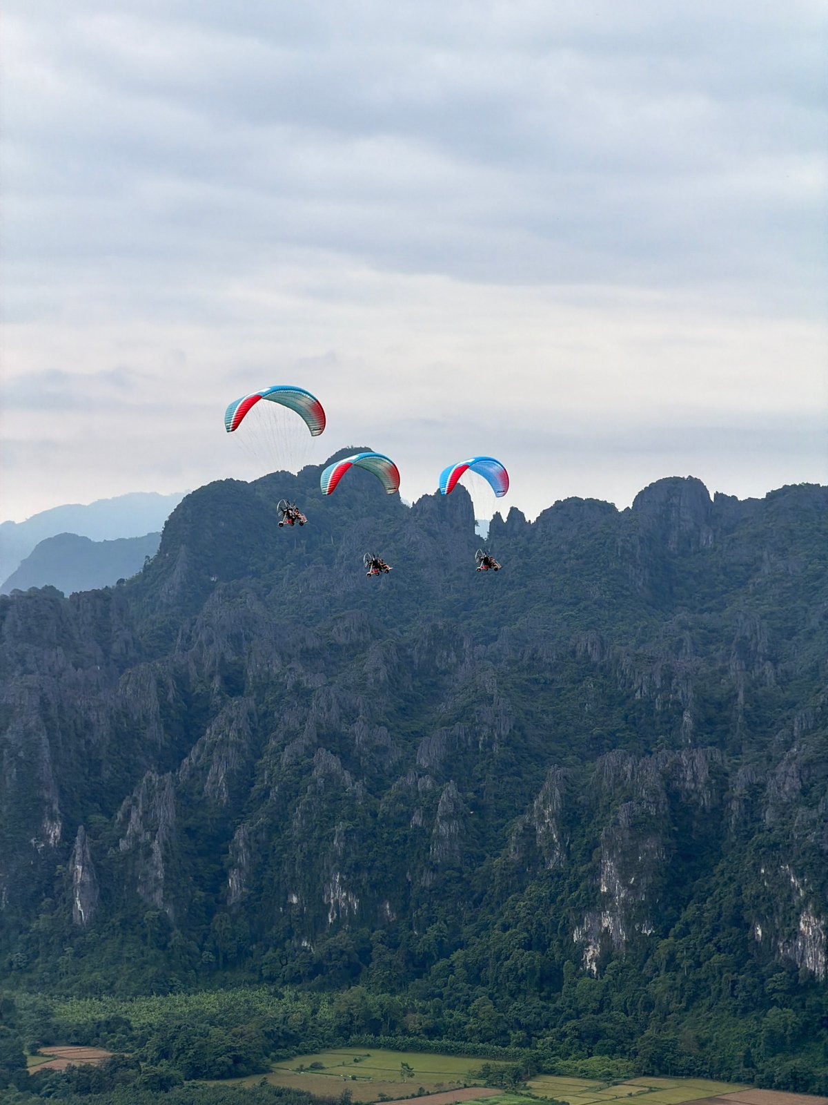 Paragliders with colorful wings over Laos mountain landscape