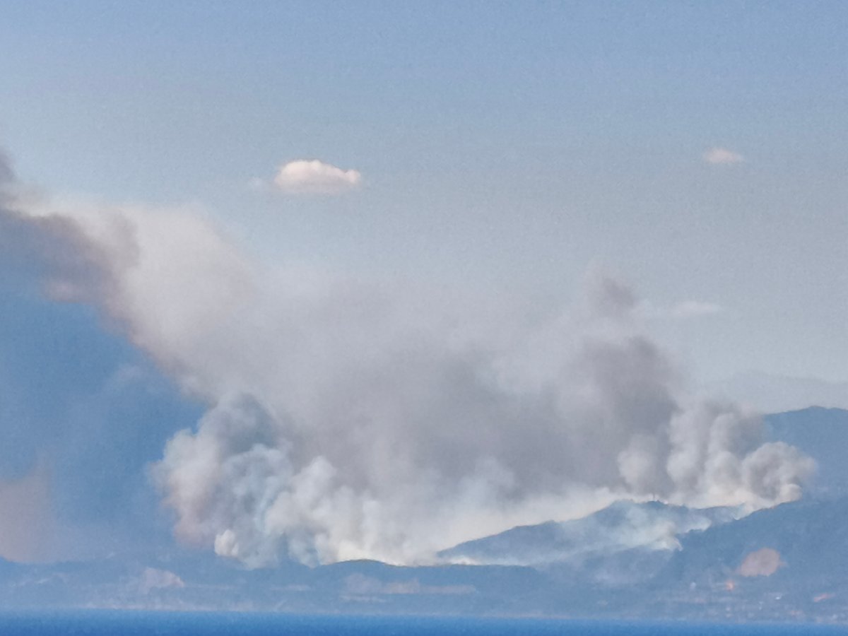 Wildfire smoke rises over Aegio's coastline, visible from the waterfront