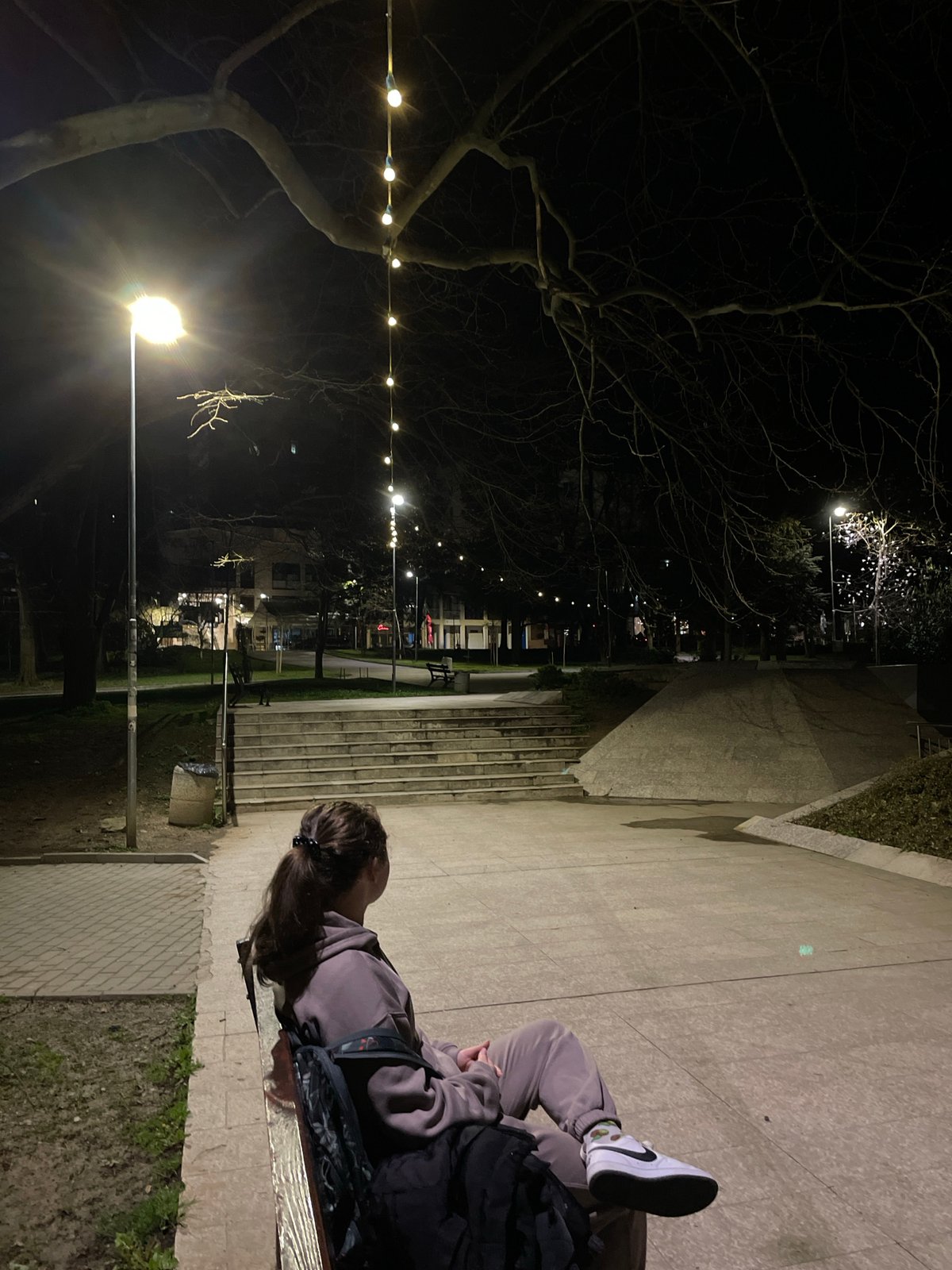 Woman sits in illuminated park during evening in Veliko Tarnovo
