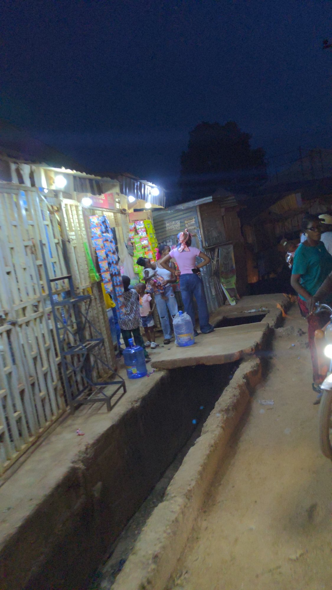 Street vendor serves customers at illuminated stand in Ado