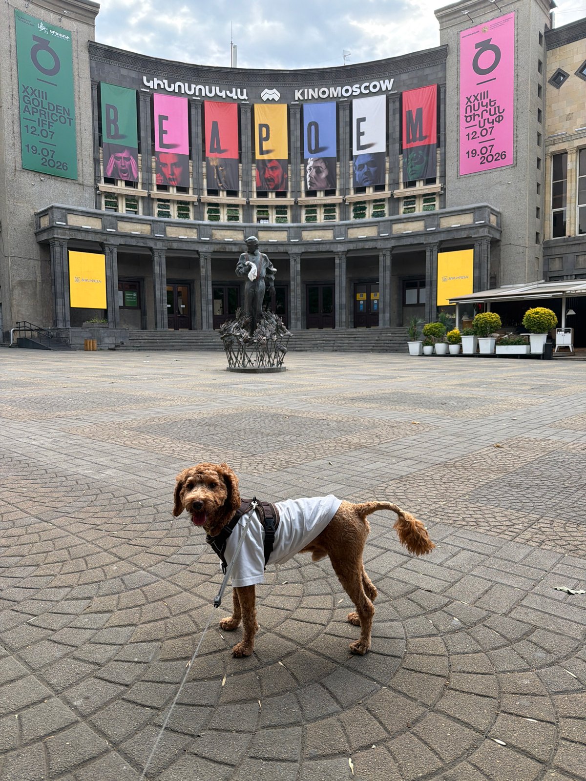 A dressed-up dog wanders a plaza with striking public sculptures