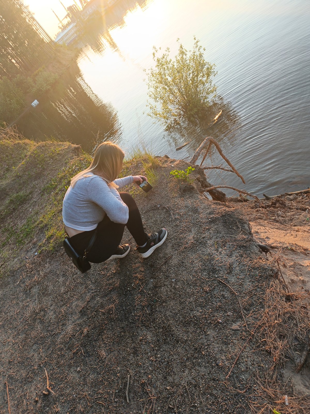 Woman crouches by water holding dark object