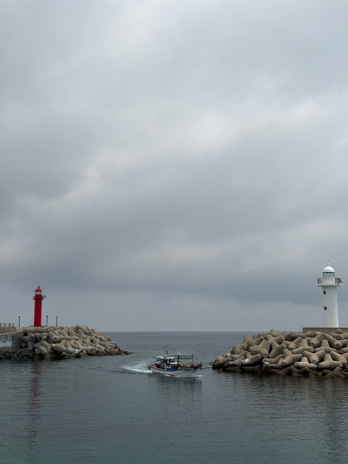 Fishing boat passes through twin-lighthouse harbor entrance in Jeju
