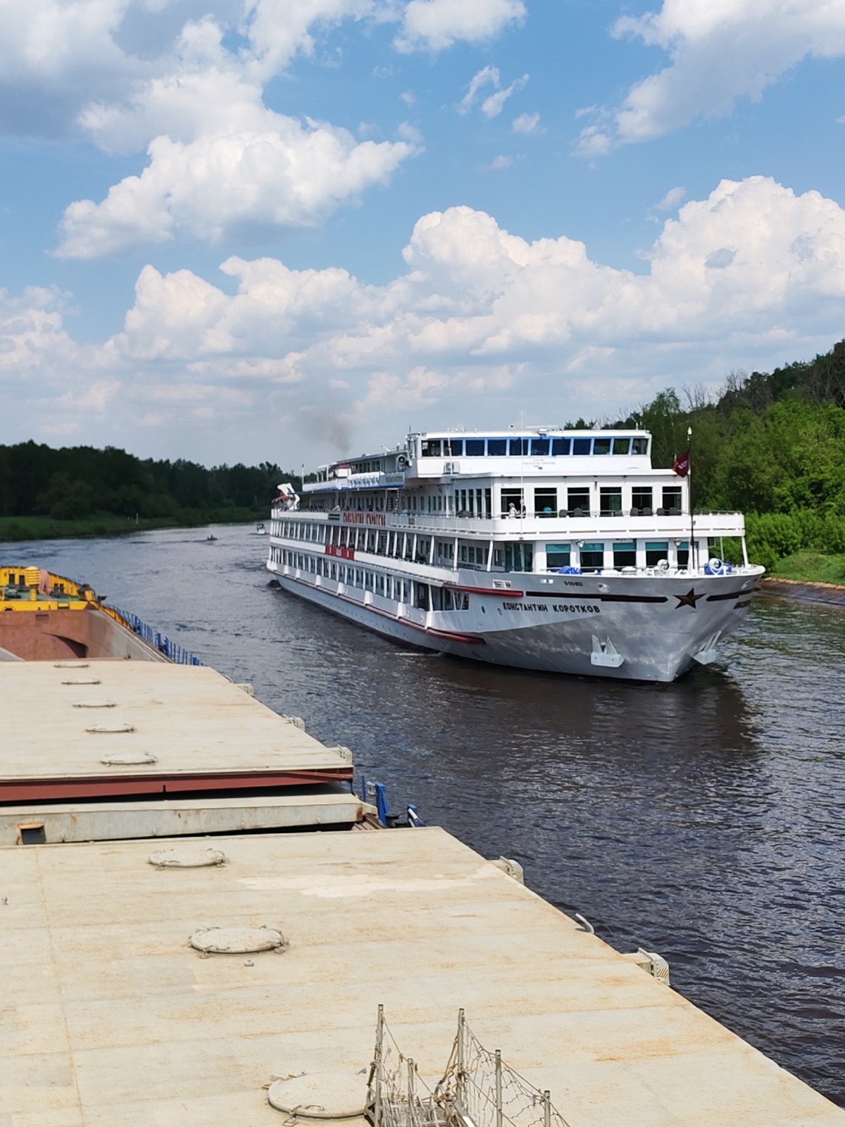 Russian cruise ships navigate tree-lined waterway, passengers observed