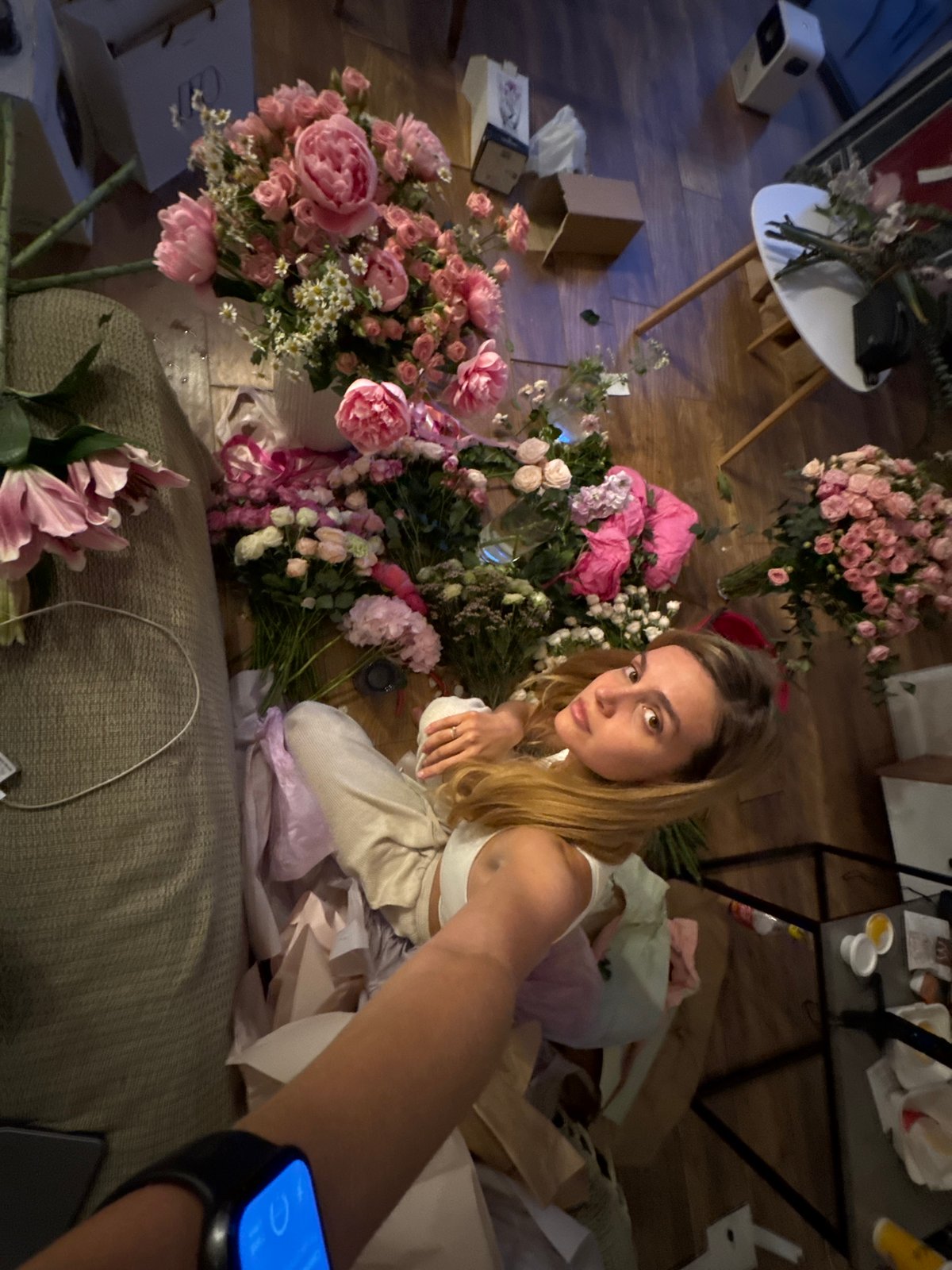 Woman prepares flower arrangements on floor with scattered blooms