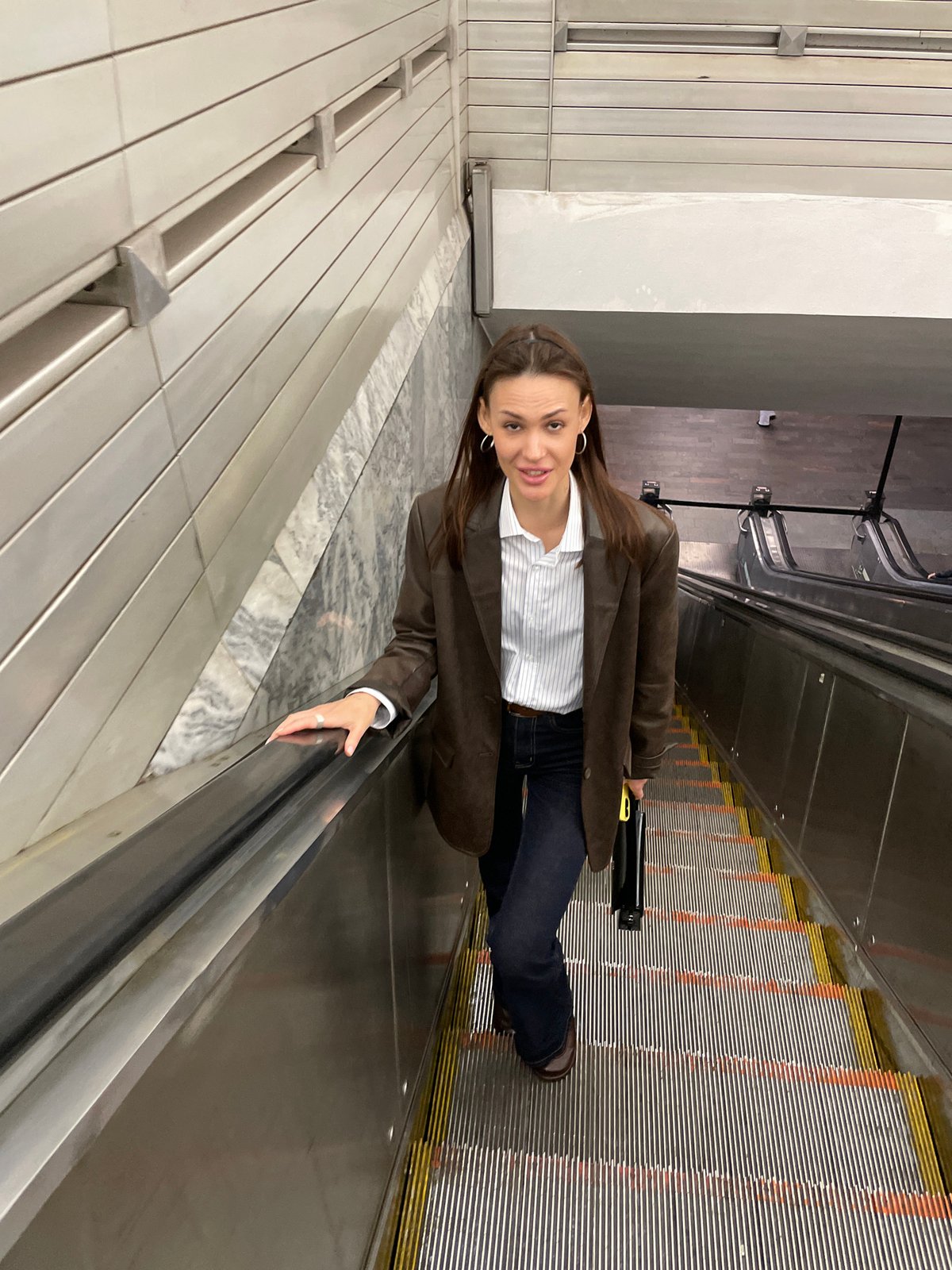 Woman rides escalator in Saint Petersburg wearing brown jacket