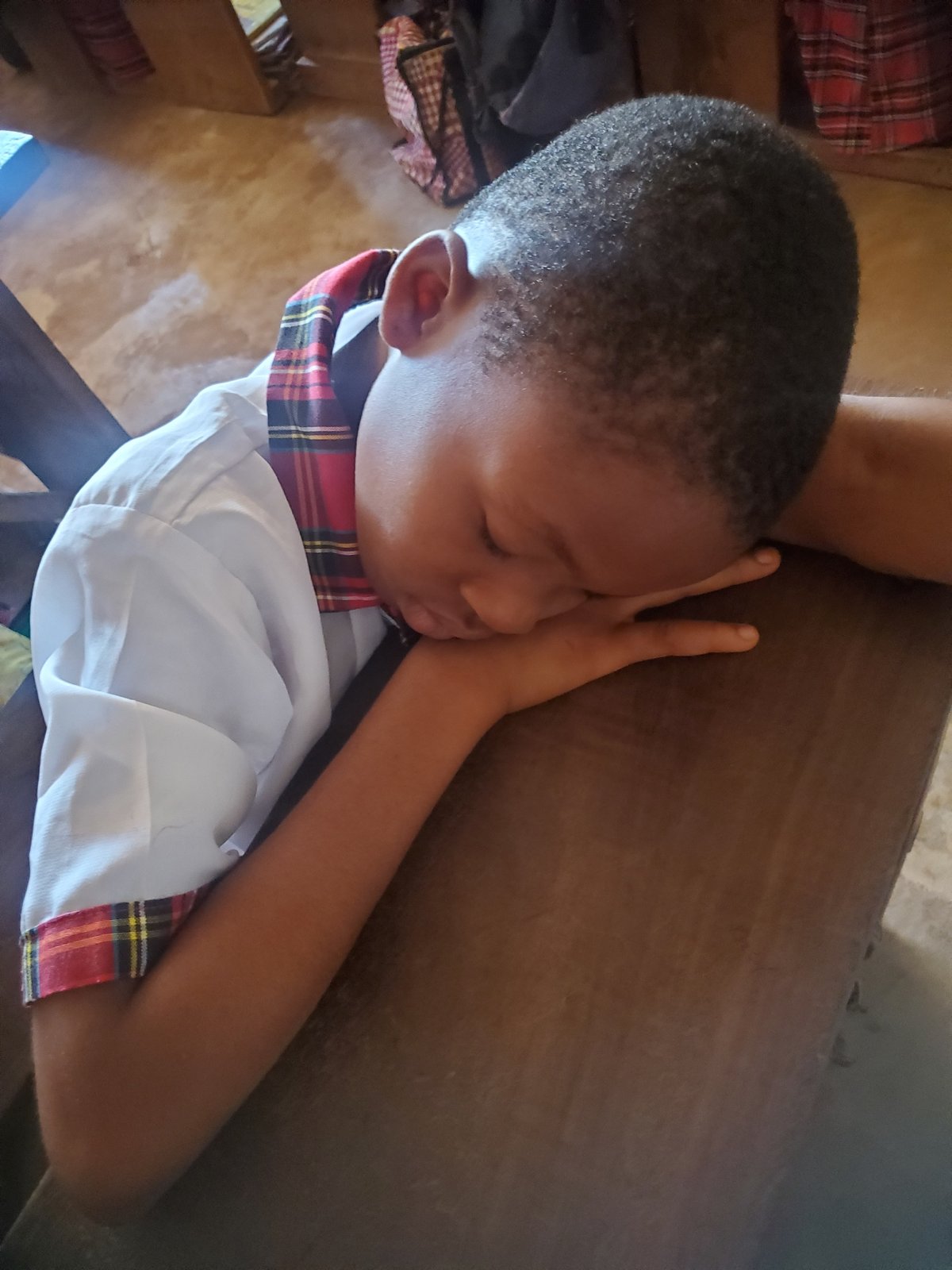 Student sleeps at desk during class in Nigerian school