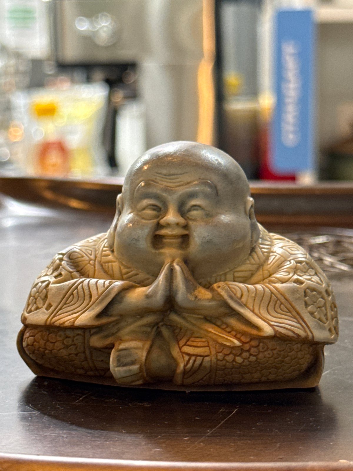 Smiling Buddha statue with carved robes on reflective surface