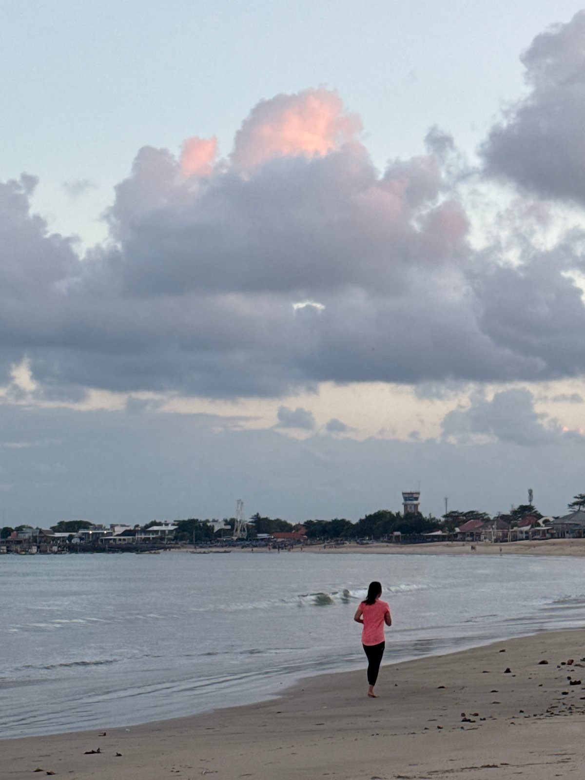 Kuta Beach at dusk: walkers, fishers, dogs, and dramatic clouds.