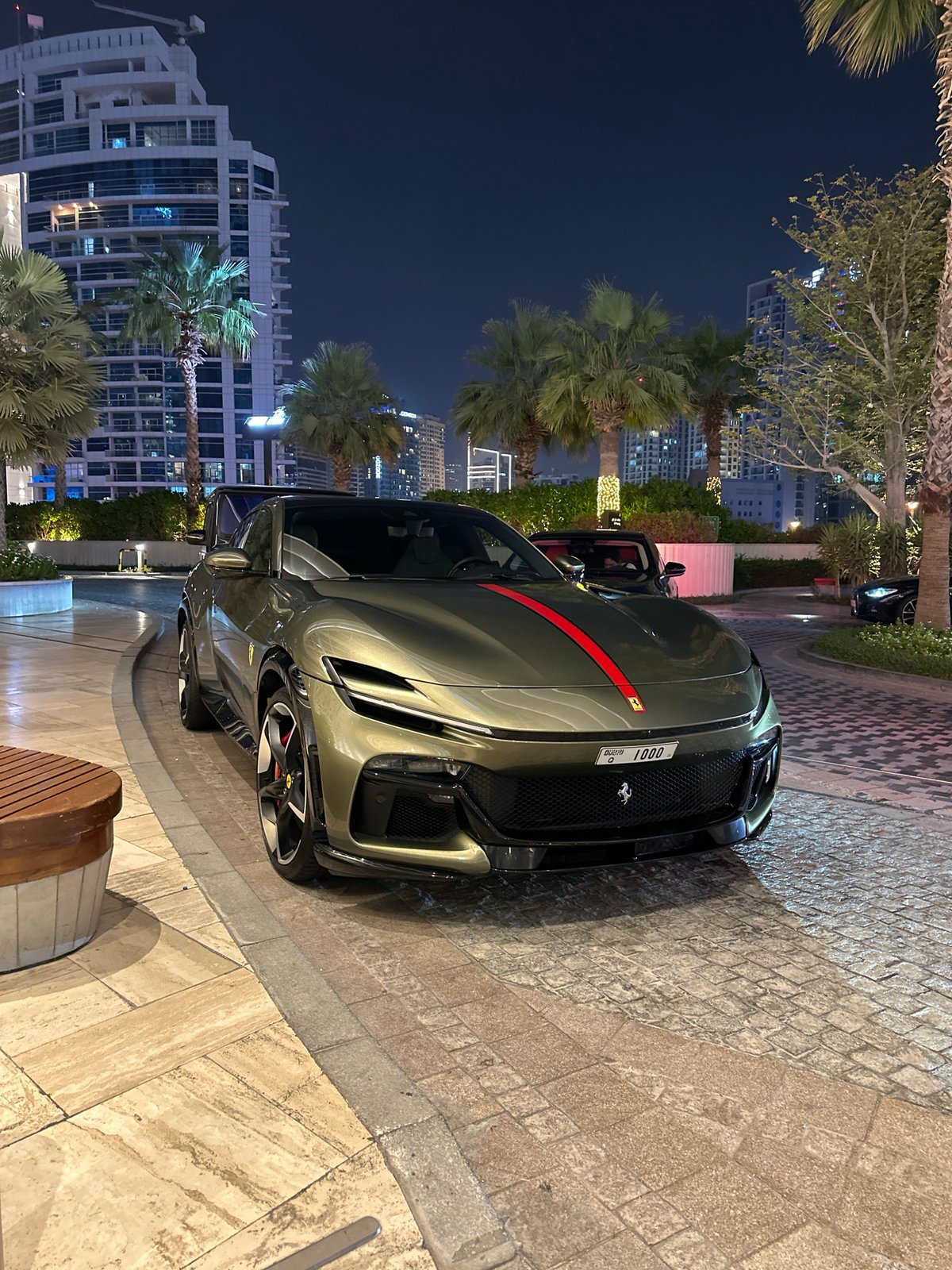 Olive green Ferrari Purosangue parked on Dubai cobblestones at night