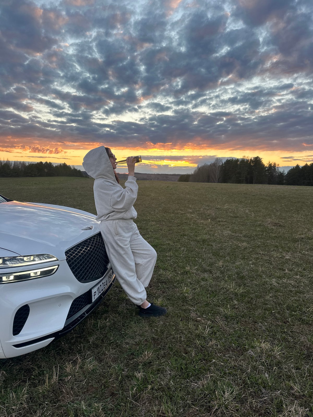 Person poses on car hood during sunset in Russian field