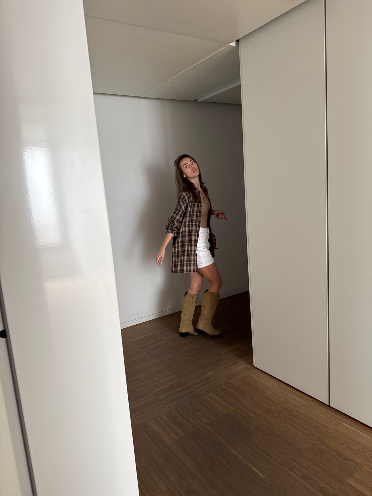 Woman photographed posing indoors in plaid shirt and cowboy boots