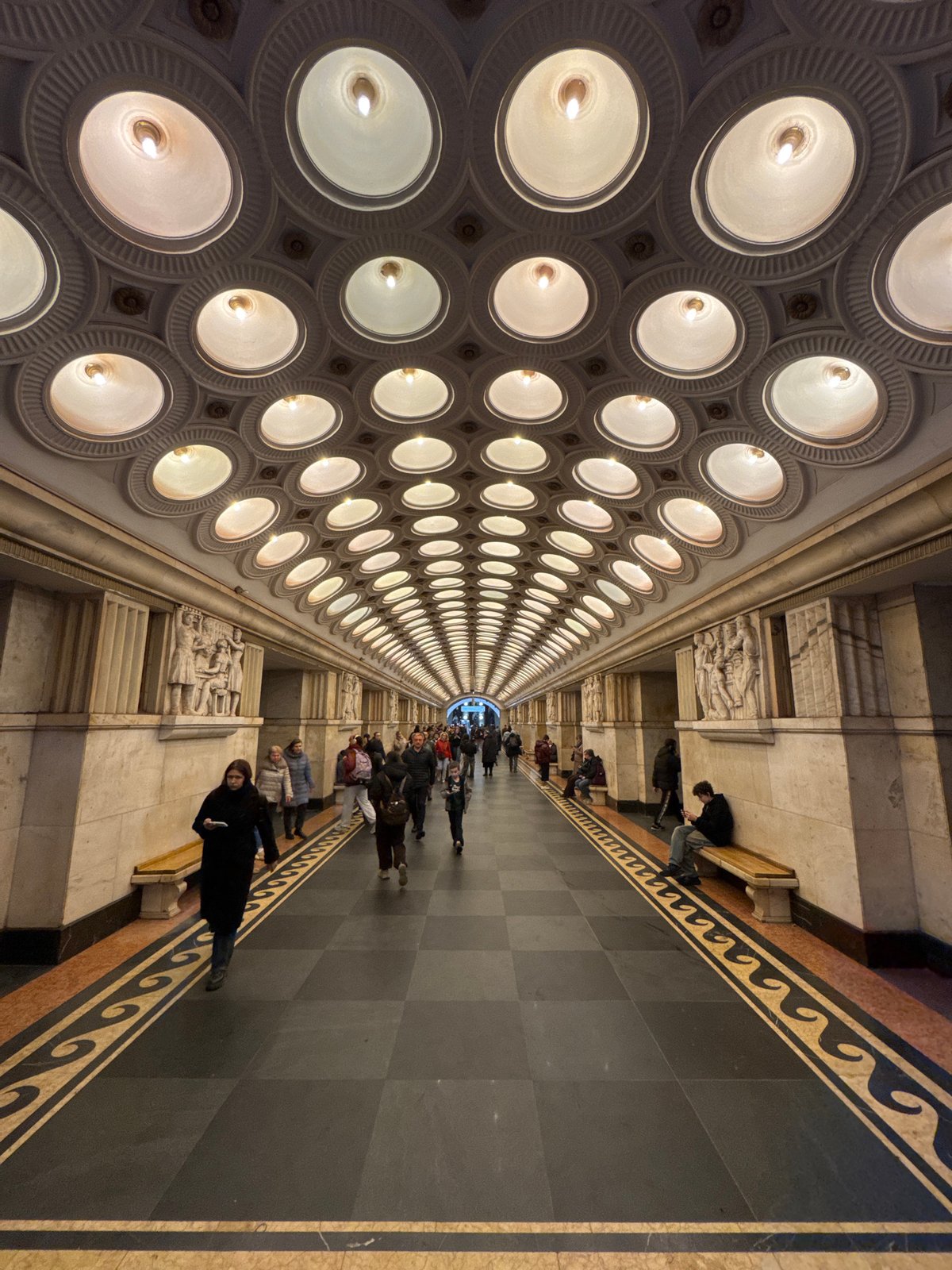 People walk through corridor with grid-pattern ceiling lighting