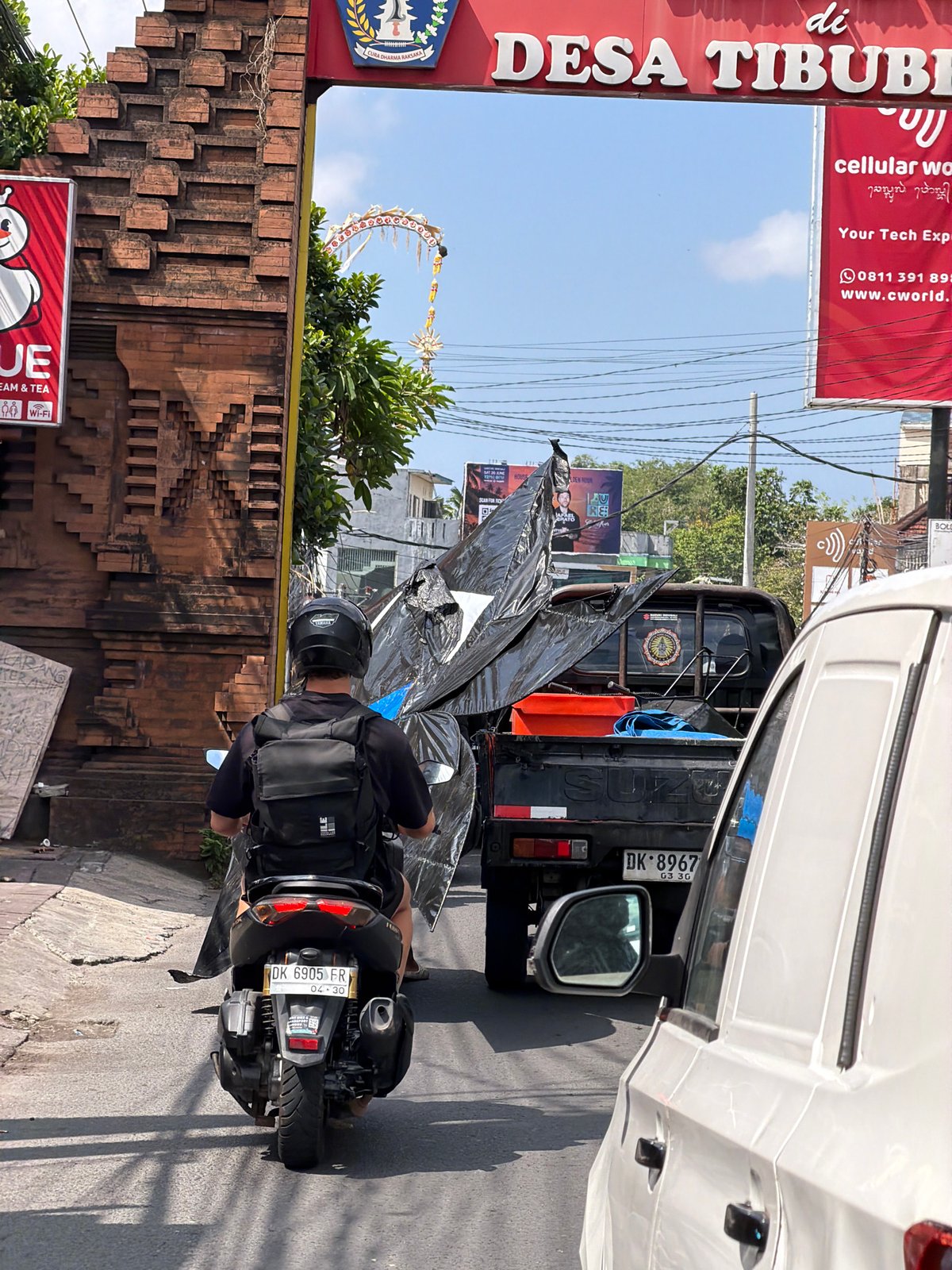 Scooter traffic rolls through a sunny North Kuta street