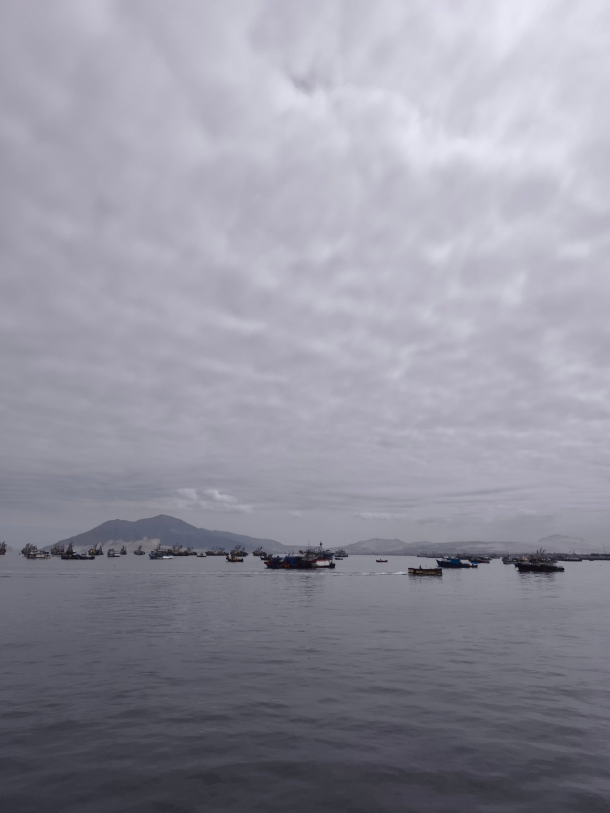 Fishing boats dot calm Chimbote harbor under overcast skies