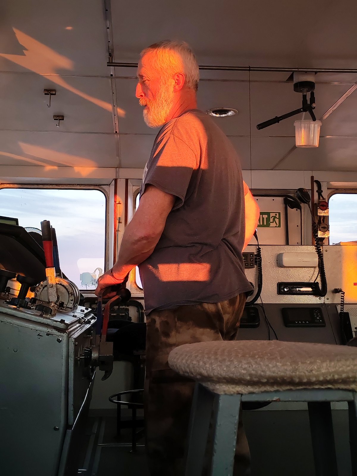 Bearded mariner navigates vessel during golden sunset over Russian waters