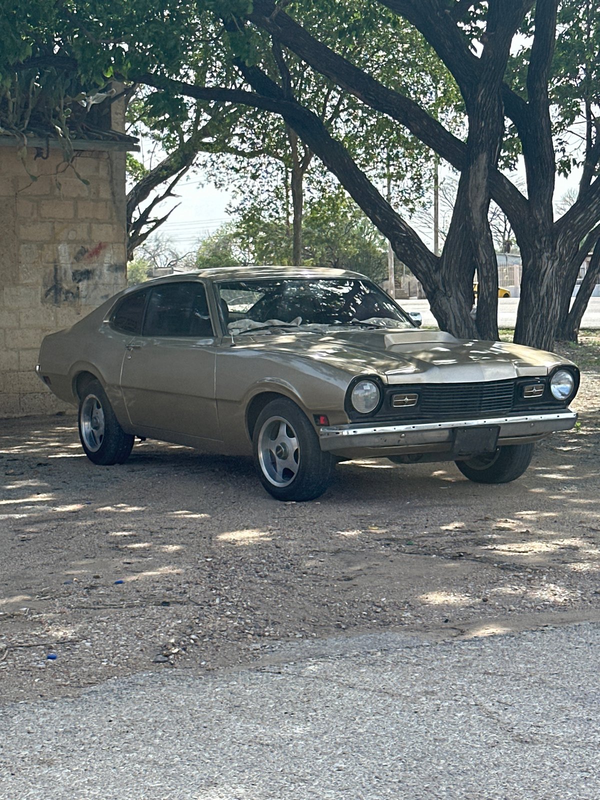 Vintage gold Ford Maverick parked under trees in Venezuela