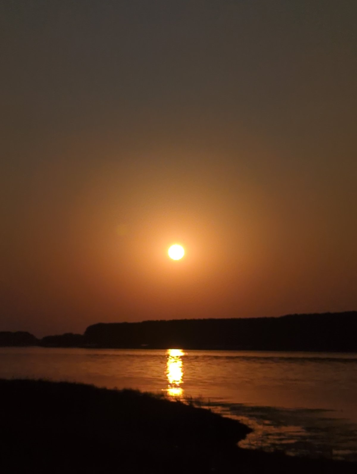 Orange sun low over calm water, sky fading to blue