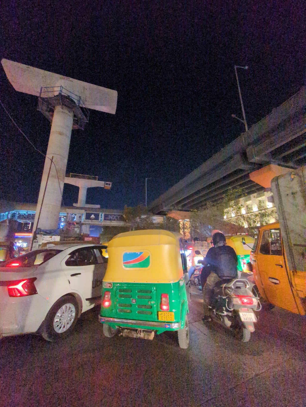 Auto-rickshaw parks beside white car on busy Bengaluru street