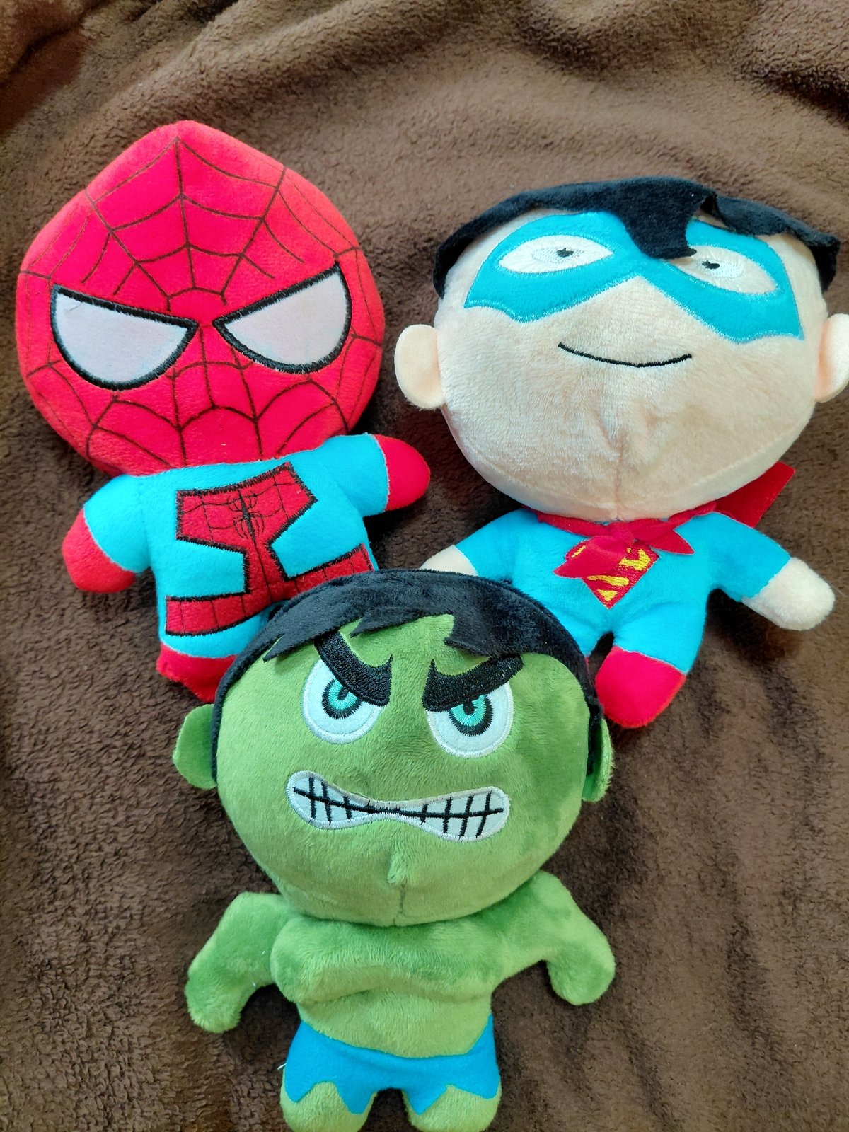 Three superhero plush toys spotted on brown surface