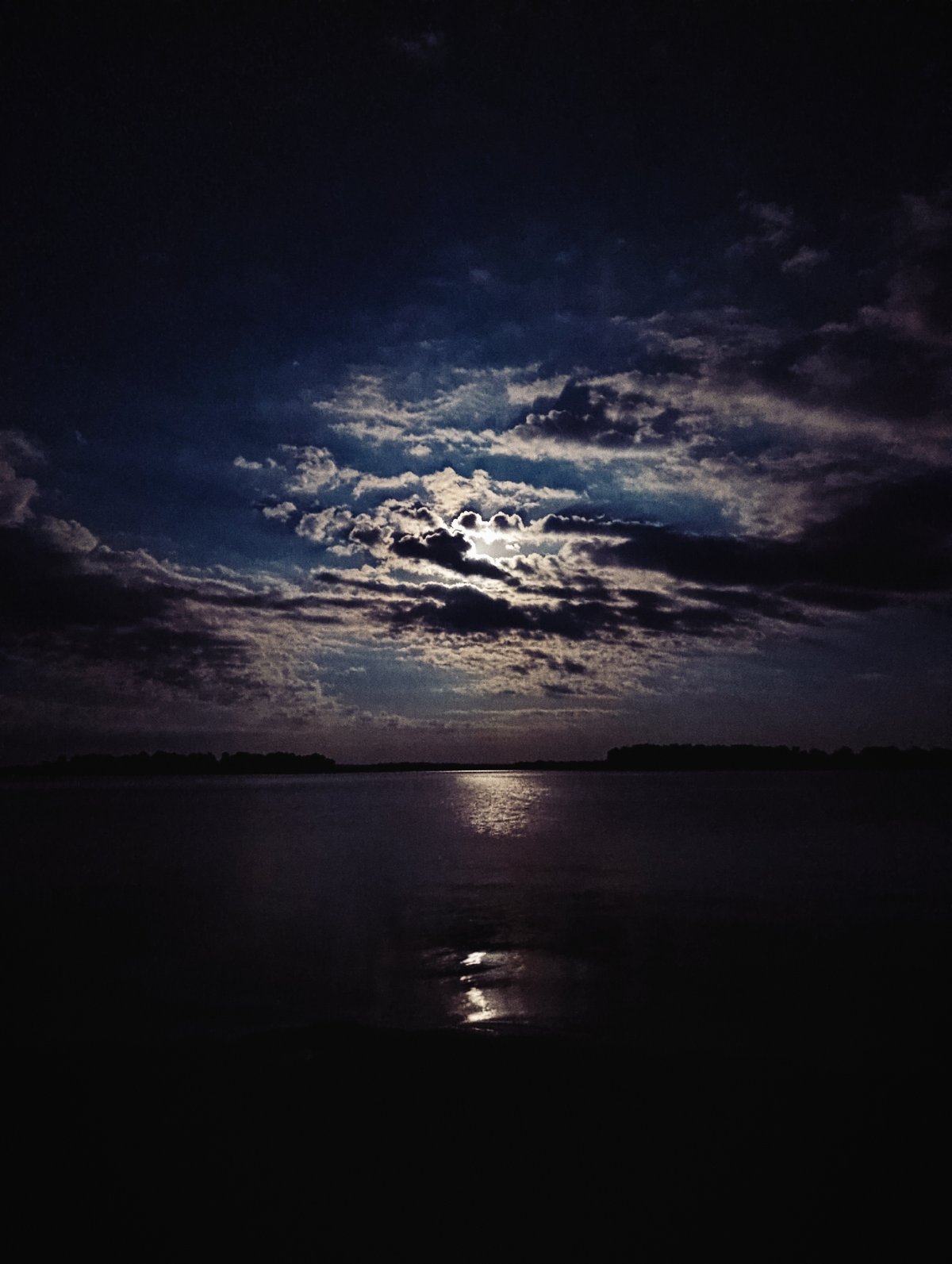 Cloudy night sky over still water, moonlight diffused