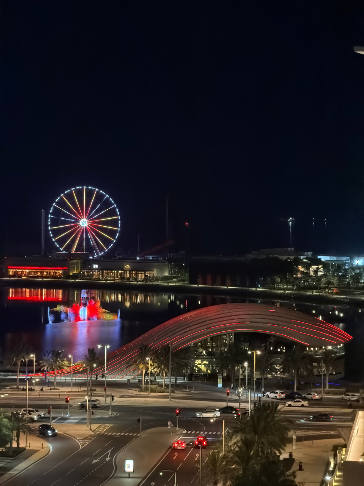 Illuminated Ferris wheel and arched bridge at an urban waterfront night