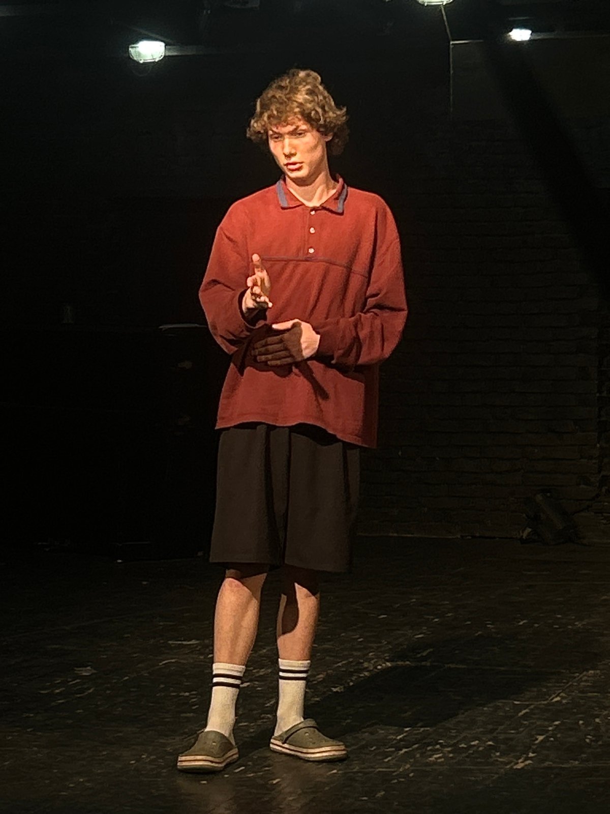 Young performer rehearses on dimly lit stage, captured by witnesses