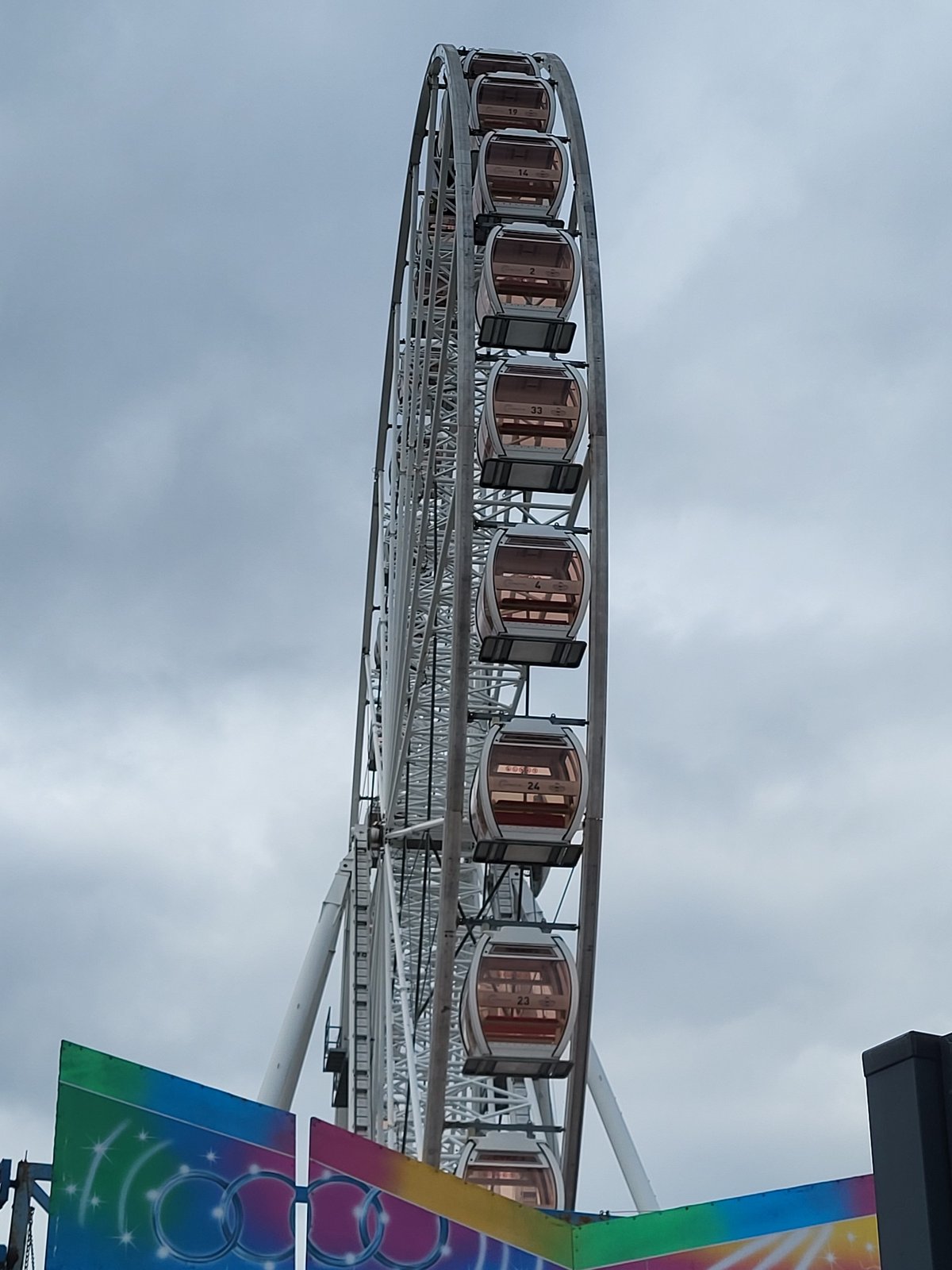 Large white Ferris wheel operates under partly cloudy skies