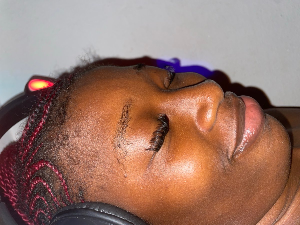 Person with braids listens to headphones under colored lights