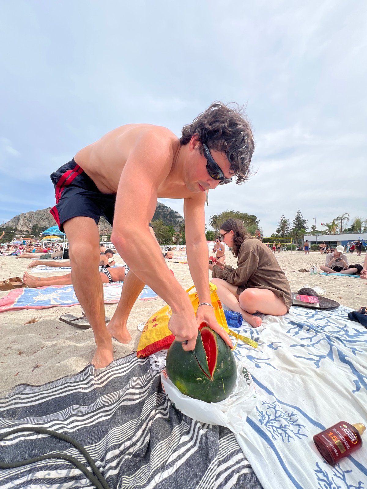 Man cuts watermelon on busy Palermo beach