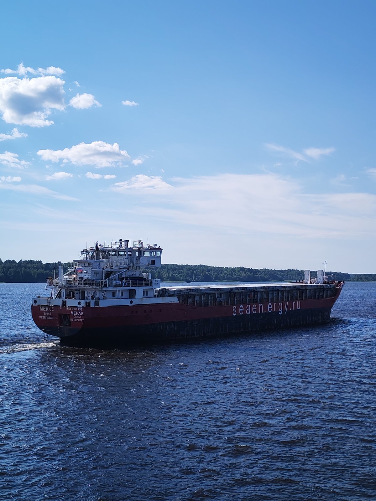 Red-hulled cargo ship MERLE sailing Russian river on clear day