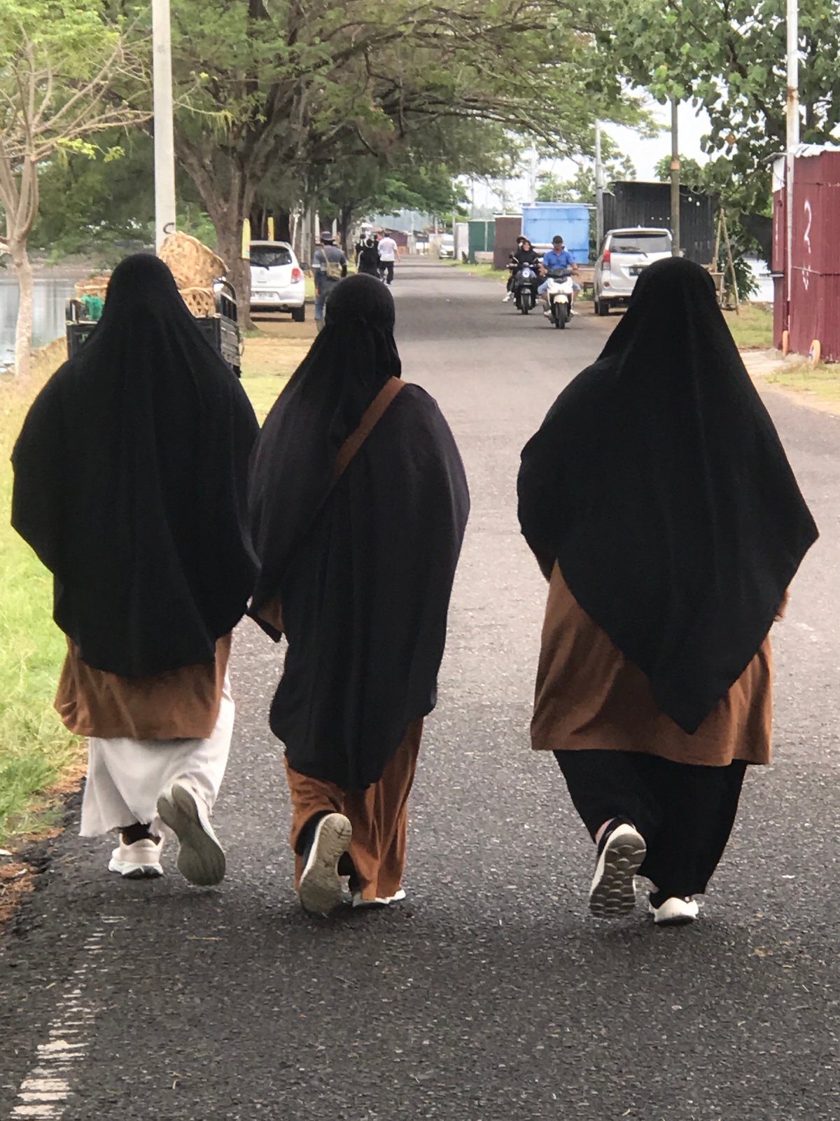 Three niqab-wearing individuals walk street in Lhokseumawe, Indonesia