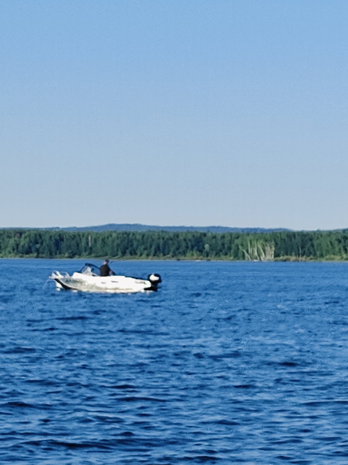 Motorboat cruising open water near forested Russian riverbank