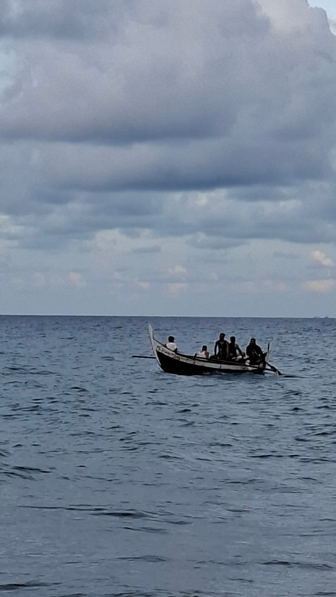 Busy morning at Lhokseumawe's Ujong Blang Beach — swimmers, boats, rocky shore
