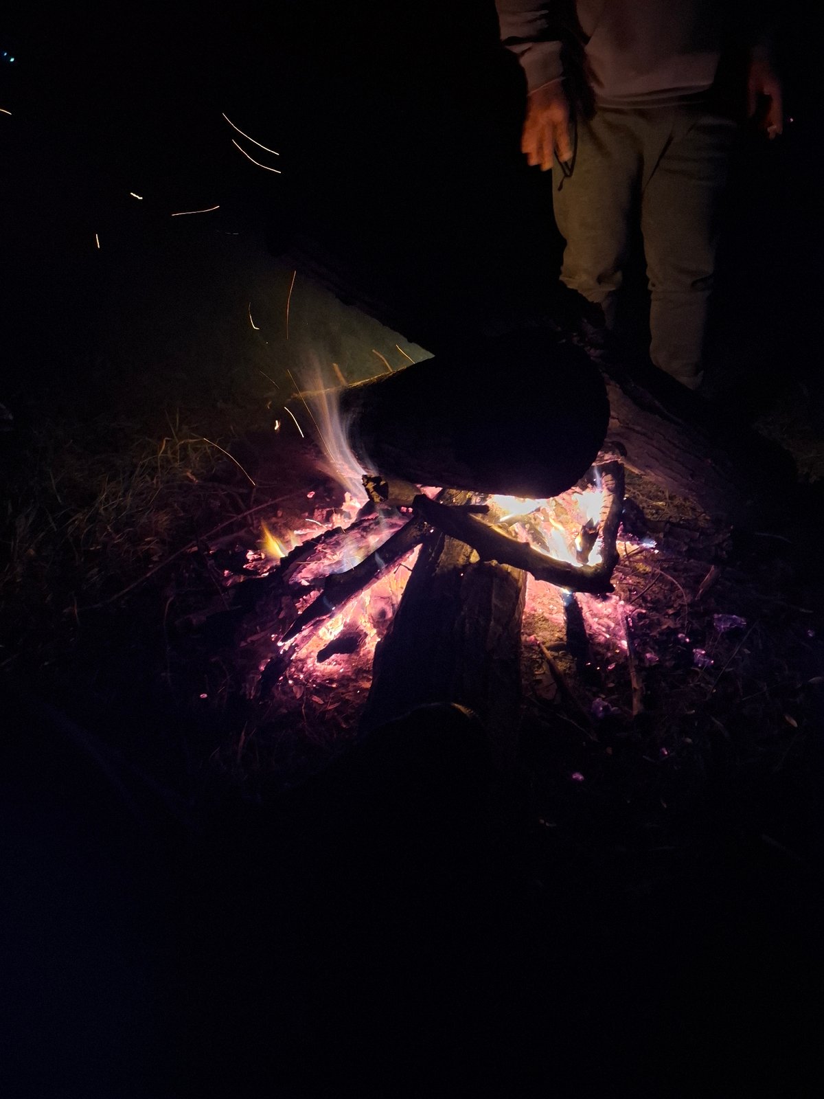 Nighttime campfire scene with person present, flames visible