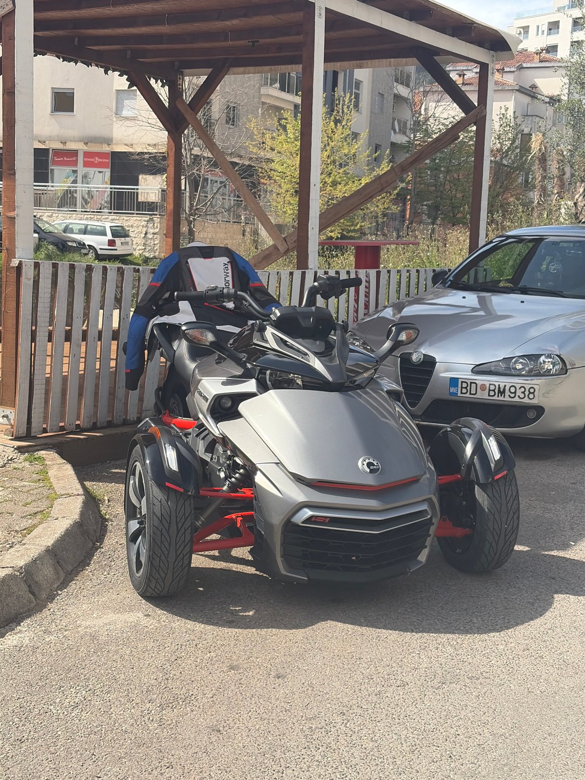 Can-Am Spyder parked with silver car near covered structure