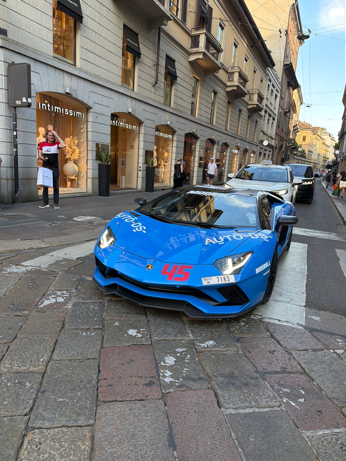 Person down on a Milan cobblestone street near shops