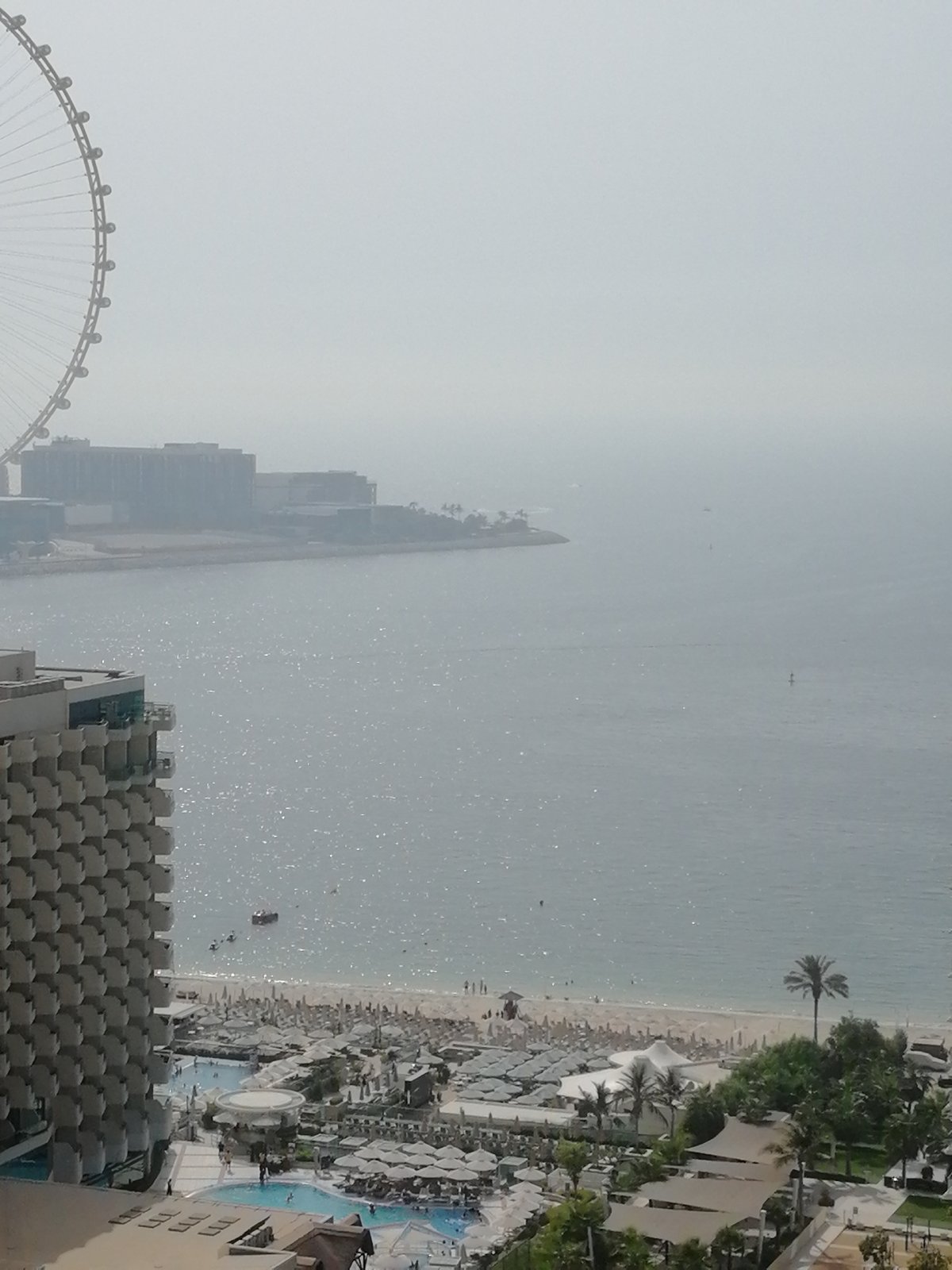 Hazy coastal panorama with Ferris wheel on Dubai's waterfront