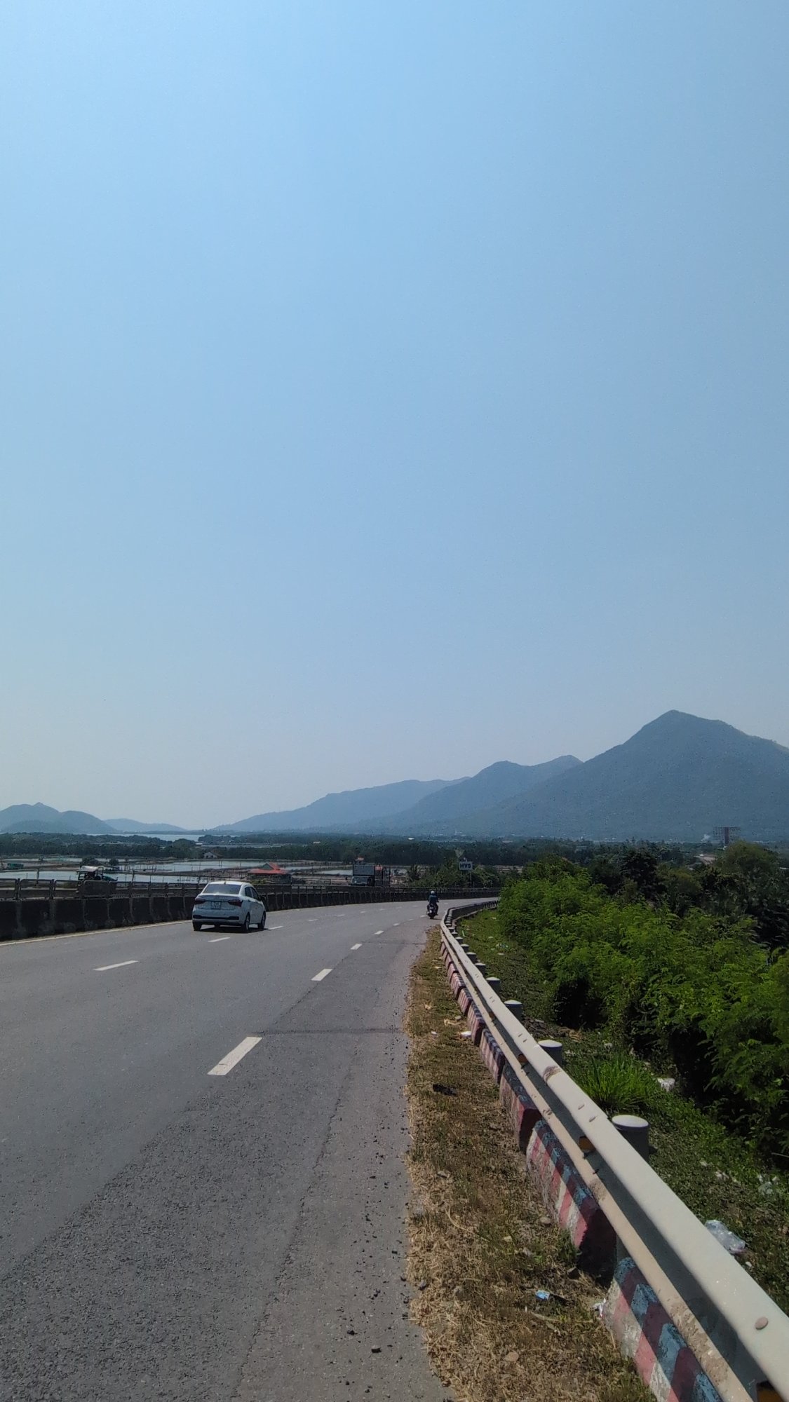 Vehicle travels Vietnamese road amid mountainous water landscape