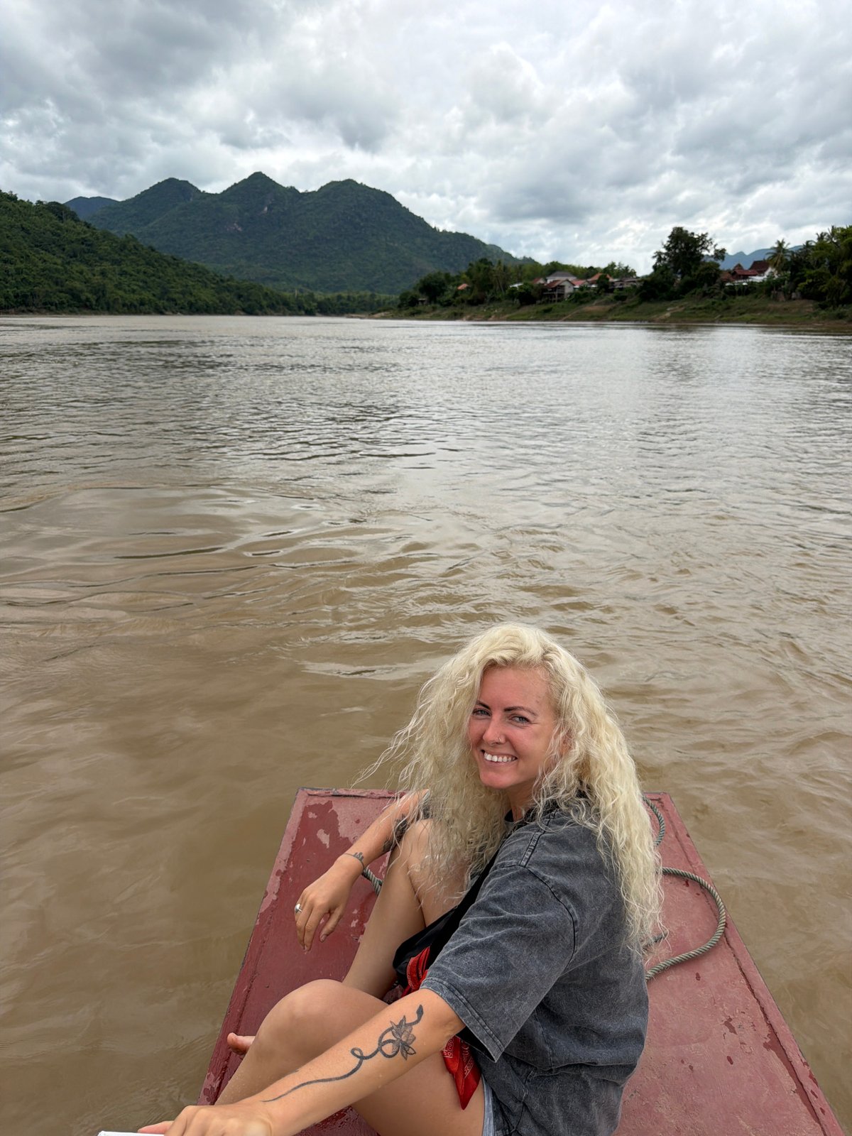 Drifting down a muddy Laotian river on a red wooden boat