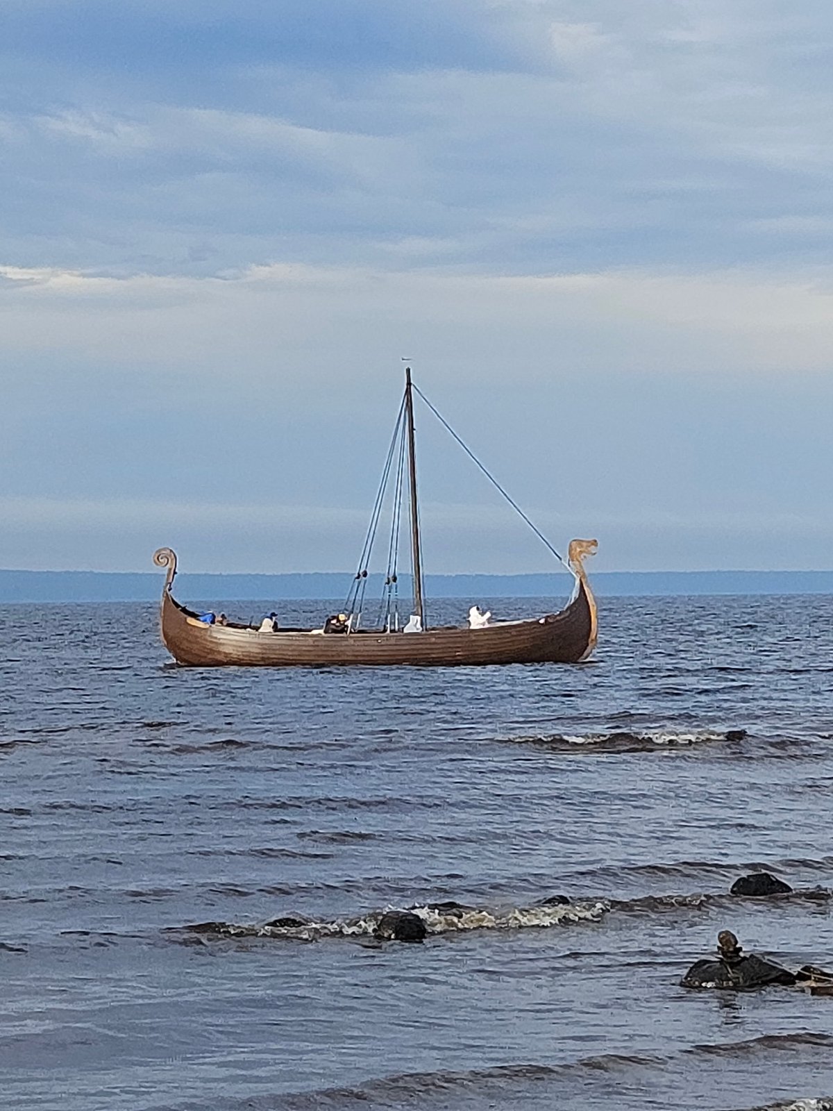 Viking longship sails past a busy waterfront on a grey day