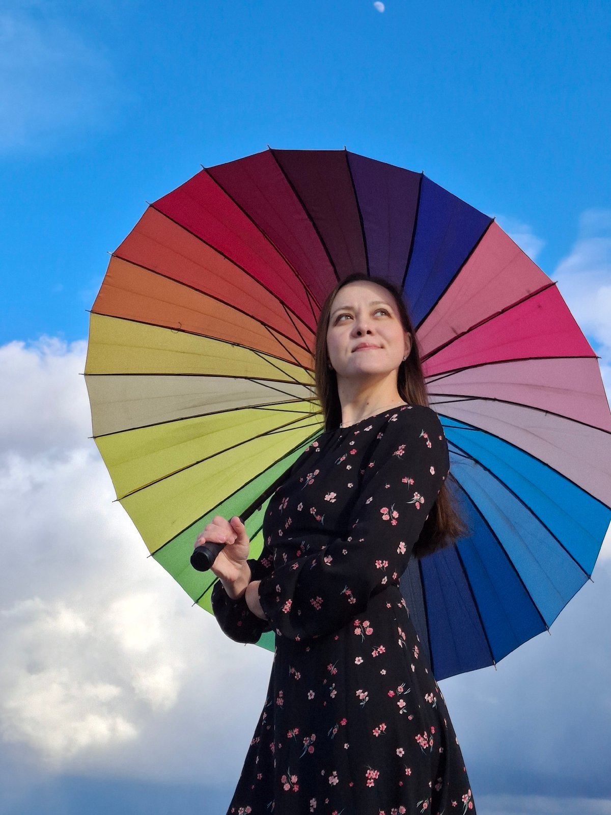 Woman poses with rainbow umbrella by waterfront in Chaikovsky