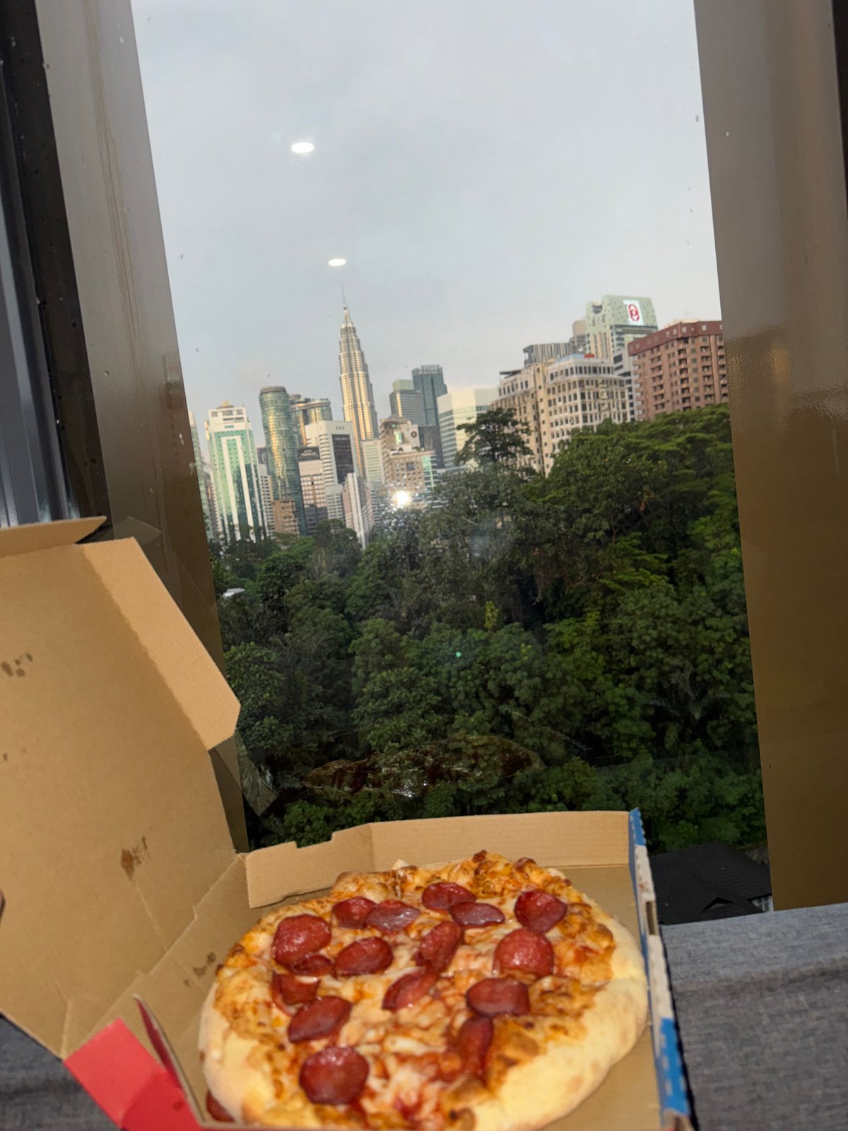 Pizza lunch documented overlooking Kuala Lumpur skyline