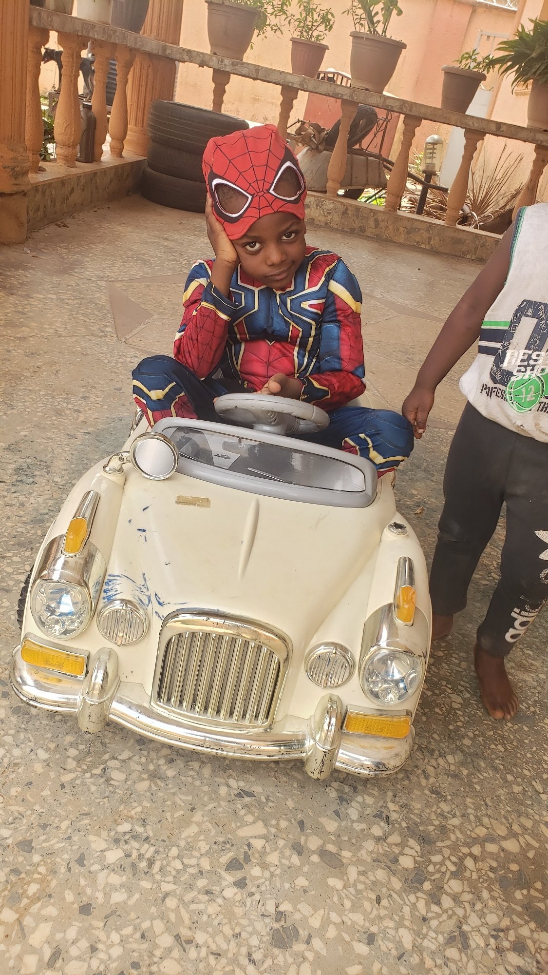 Child in Spiderman costume poses in toy car