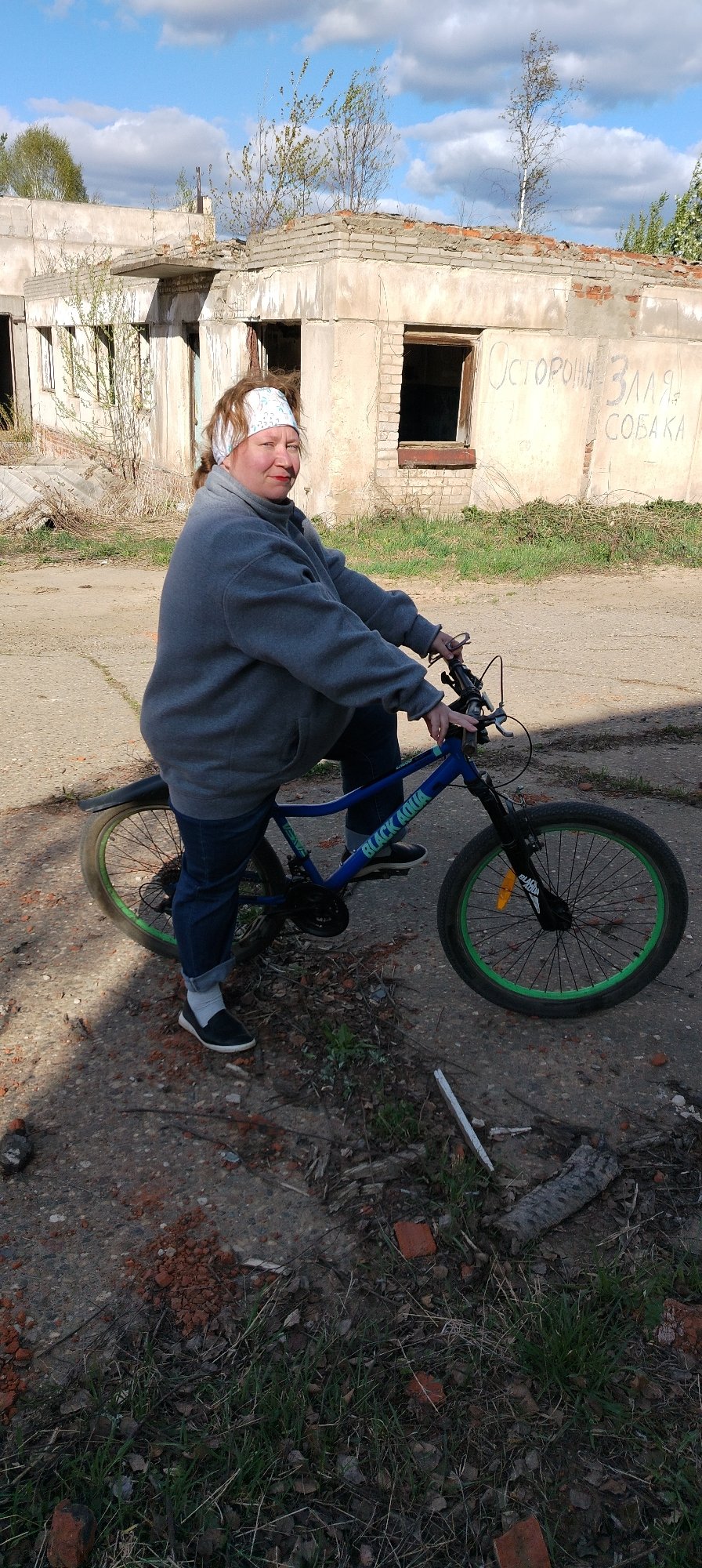 Woman poses with bicycle near ruins in Зипуново, Russia