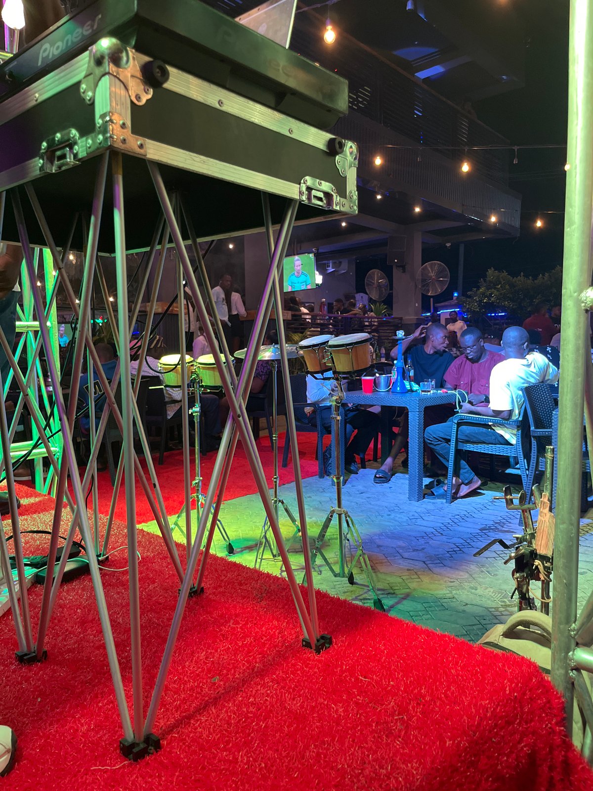 Outdoor bar night with DJ set, live drums, and string lights