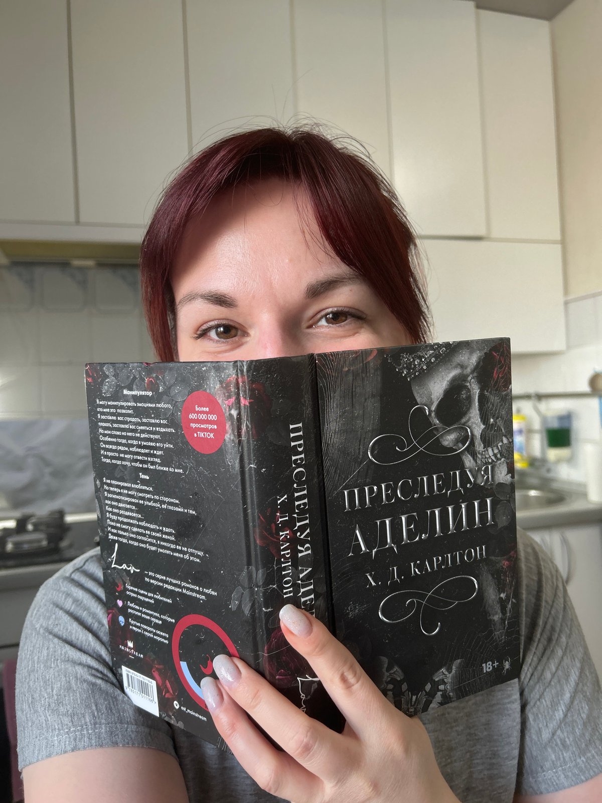 Woman reads gothic novel while eating and drinking in kitchen