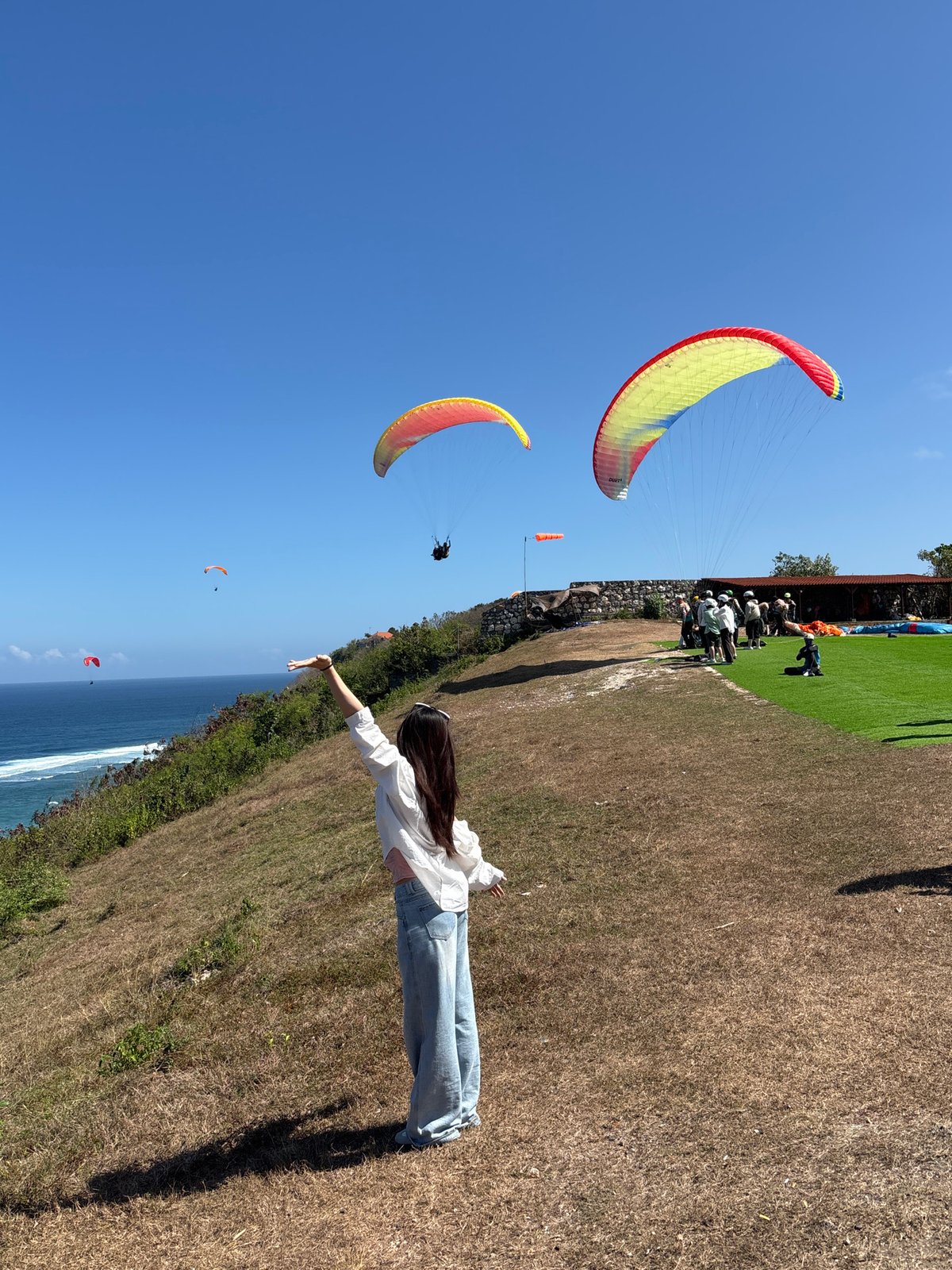 Paragliders soar over Kuta Selatan's coastal cliffs on a clear morning
