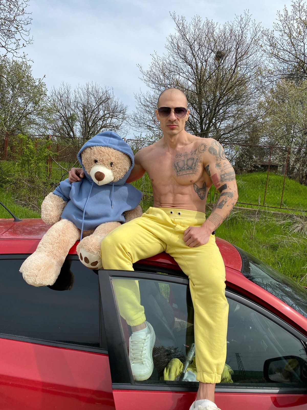 Tattooed man poses with teddy bear on car in Bulgaria