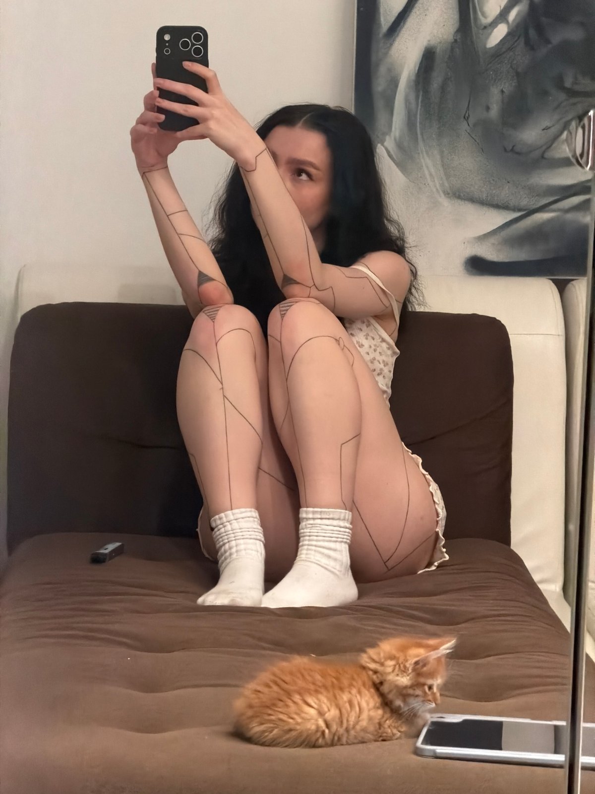 Woman takes selfies with orange cat on sofa